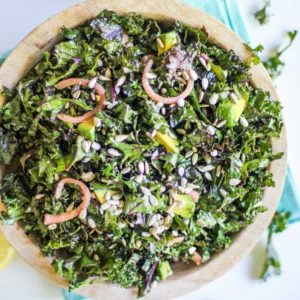 Large bowl full of massaged kale salad with pickled red onions and avocado.