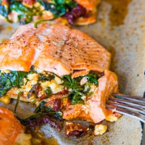 Mediterranean Stuffed Salmon on a large rimmed baking sheet, fresh out of the oven with a fork taking a bite out of it.