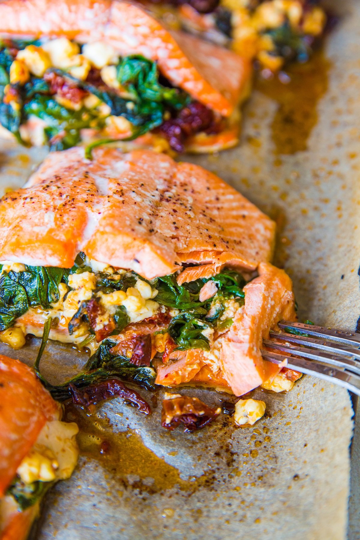 Mediterranean Stuffed Salmon on a large rimmed baking sheet, fresh out of the oven with a fork taking a bite out of it.