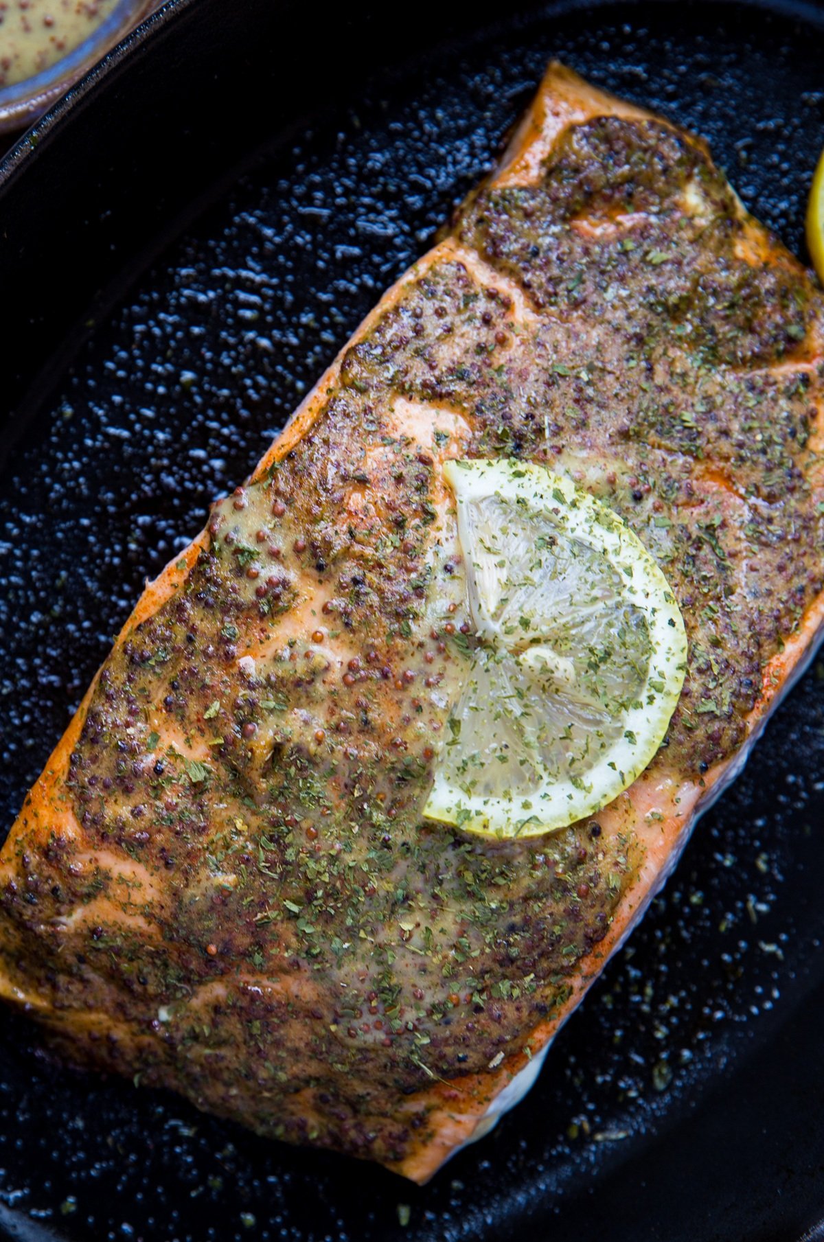 Mustard salmon fresh out of the oven in a baking dish with a slice of lemon on top, ready to serve.