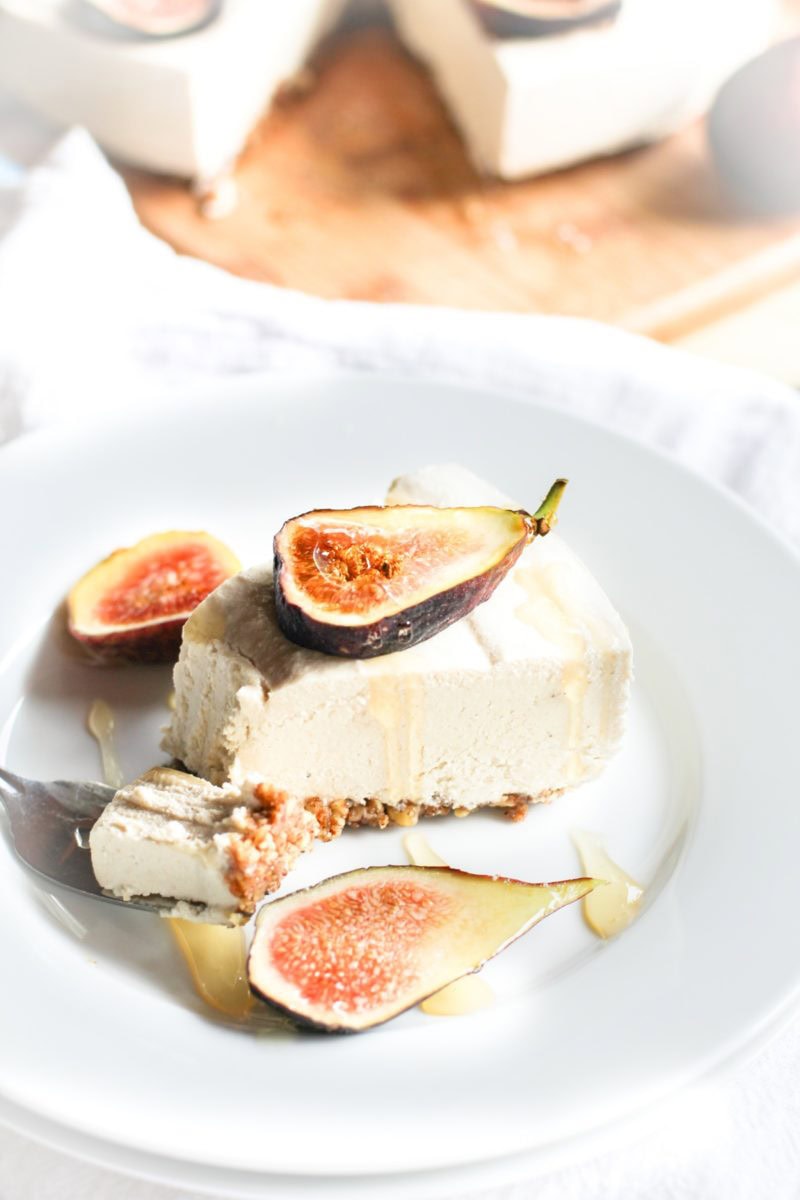Slice of no-bake dairy-free cheesecake on a plate with sliced figs and a drizzle of pure maple syrup.