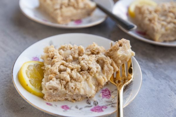 Lemon Crumble Bar on a plate with a bite taken out with a fork.