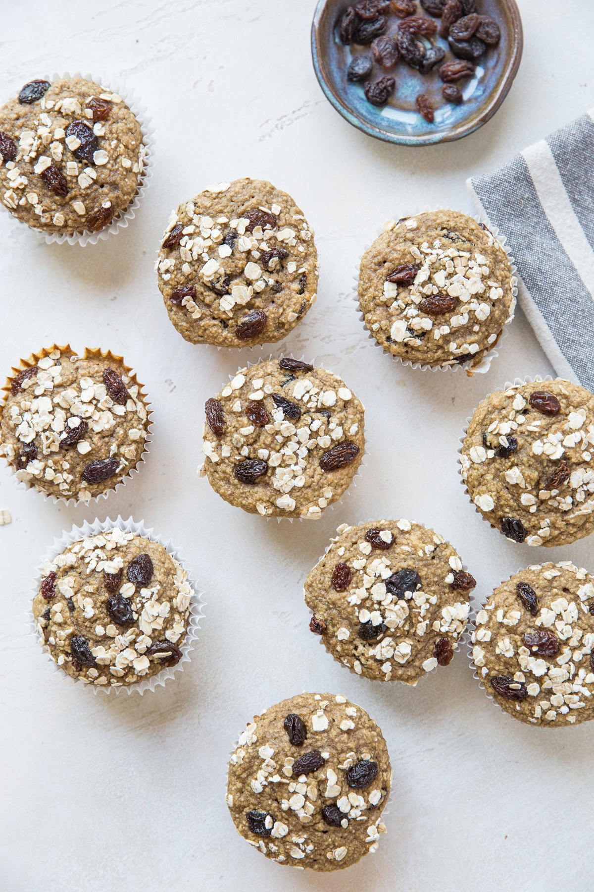 Flourless Gluten-Free Oatmeal Raisin Muffins sitting on a white background with a little bowl of raisins and a napkin to the side.