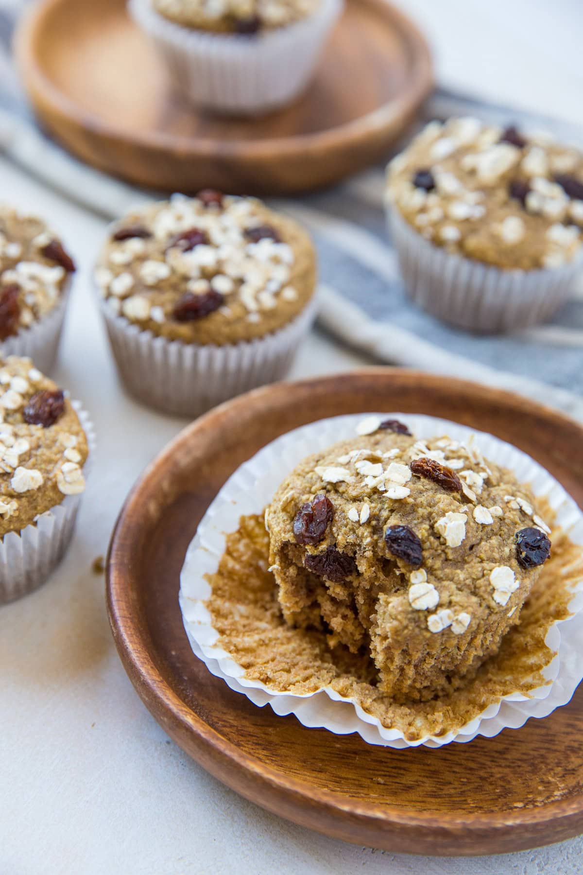 oatmeal muffin on a wooden plate with a bite taken out and the rest of the muffins in the background.