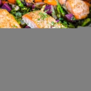 large pan of roast salmon and vegetables, ready to eat fresh out of the oven. Salmon filets sit on top of the roasted vegetables.