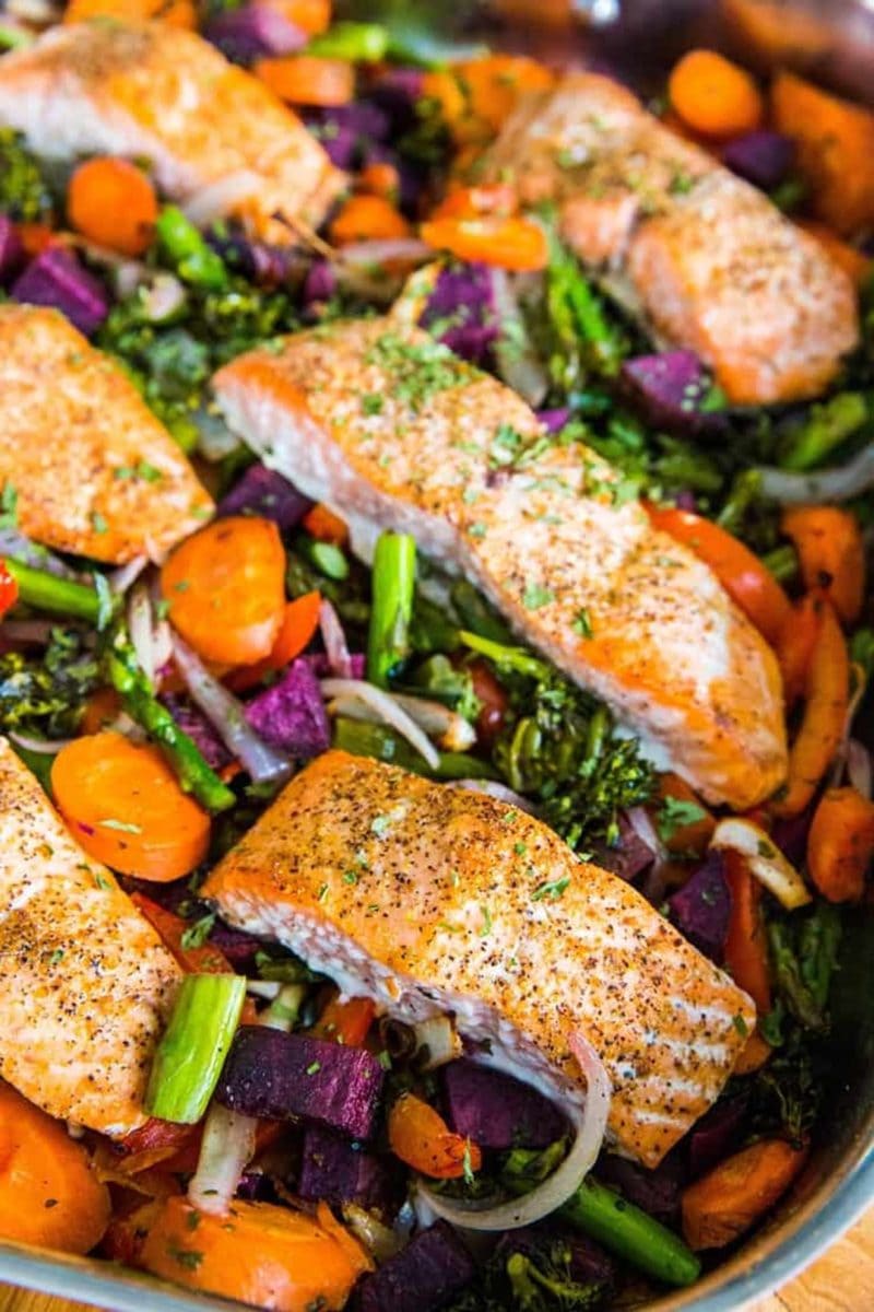large pan of roast salmon and vegetables, ready to eat fresh out of the oven. Salmon filets sit on top of the roasted vegetables.