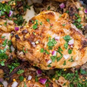 grilled orange ginger chicken thighs in a large casserole dish with chopped red onions, red pepper flakes, and parsley sprinkled on top.
