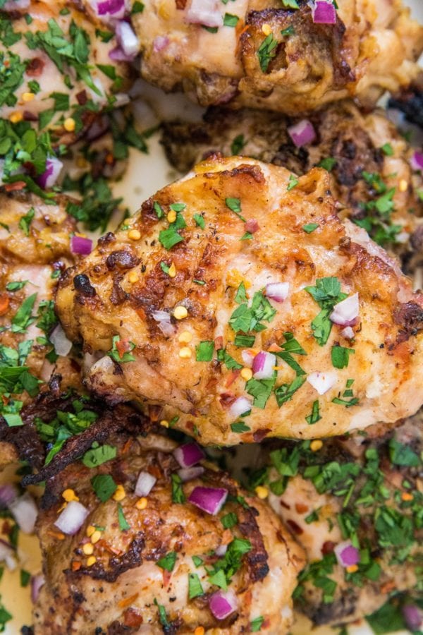grilled orange ginger chicken thighs in a large casserole dish with chopped red onions, red pepper flakes, and parsley sprinkled on top.