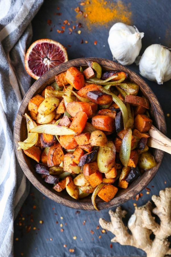 Wooden bowl full of roasted root vegetables with fresh ginger to the side.