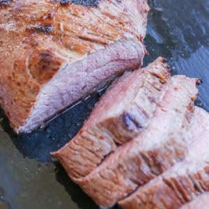 cutting board with slices of roast tri tip in its juices, ready to serve.
