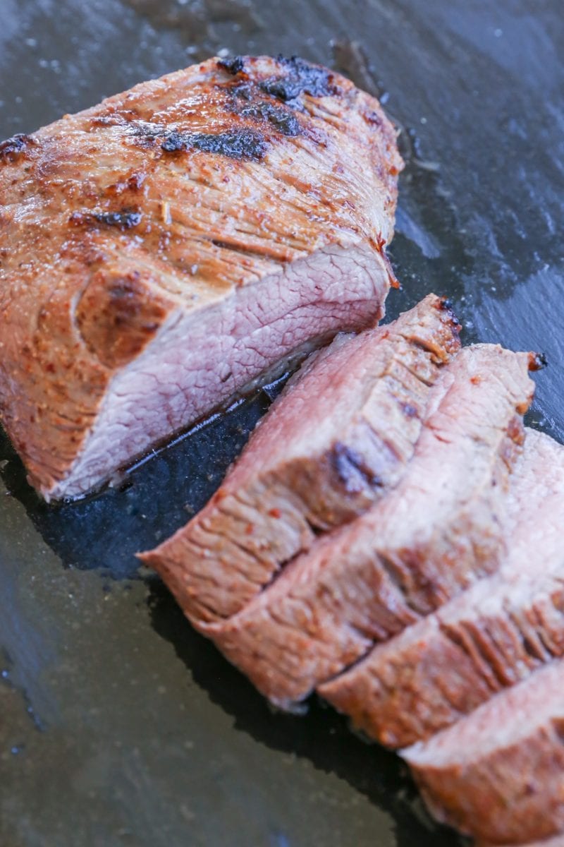 cutting board with slices of roast tri tip in its juices, ready to serve.