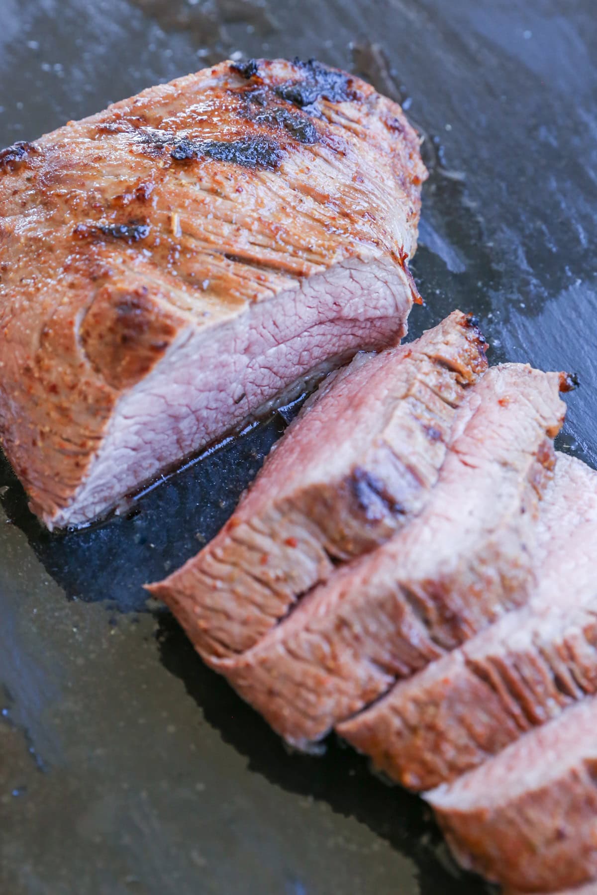 cutting board with slices of roast tri tip in its juices, ready to serve.