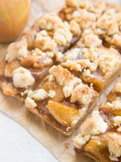 Sheet of parchment paper with gluten-free apple pie bars cut into slices. A fresh apple to the side.