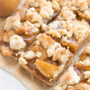 Sheet of parchment paper with gluten-free apple pie bars cut into slices. A fresh apple to the side.