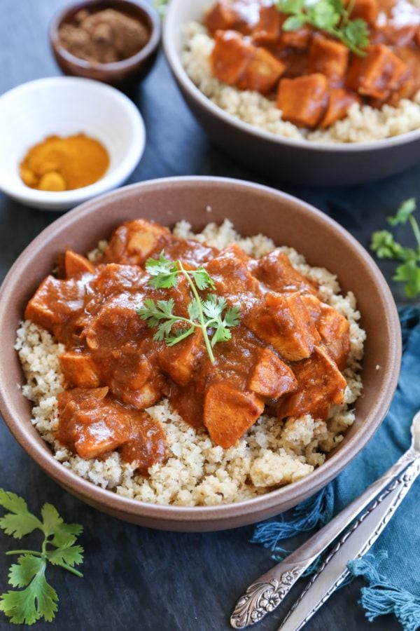 Two ceramic bowls full of butter chicken on top of cauliflower rice with forks to the side.