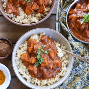 Two bowls full of paleo butter chicken with cauliflower rice with spices and a decorative napkin to the side.
