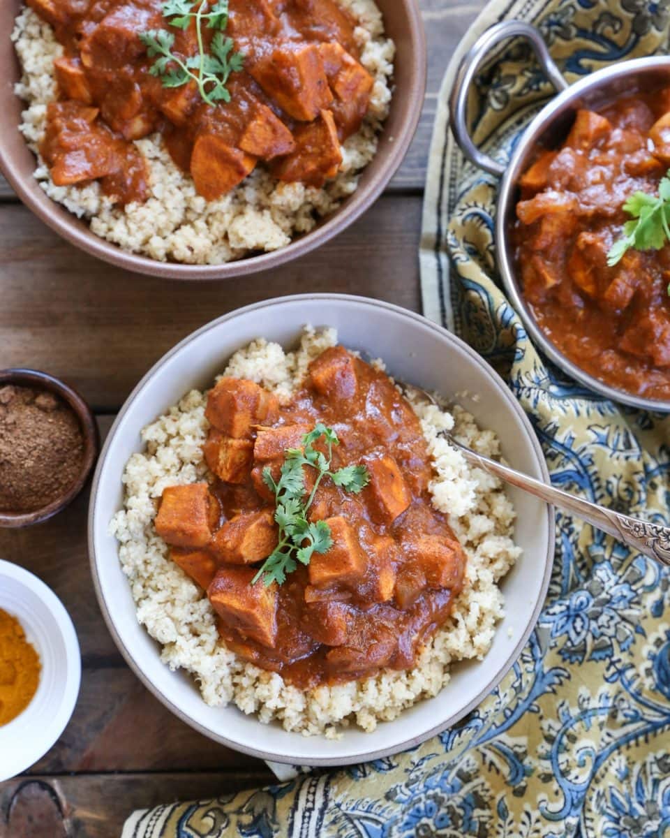 Two bowls full of paleo butter chicken with cauliflower rice with spices and a decorative napkin to the side.