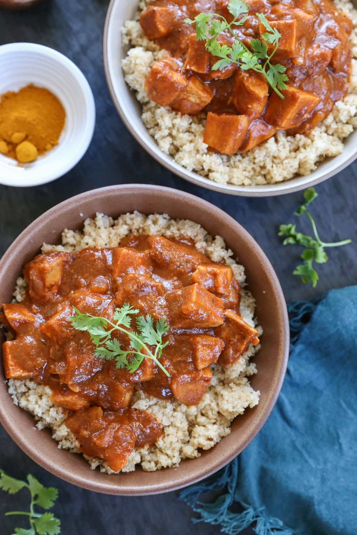 Large bowls full of butter chicken on top of cauliflower rice and a blue napkin to the side.
