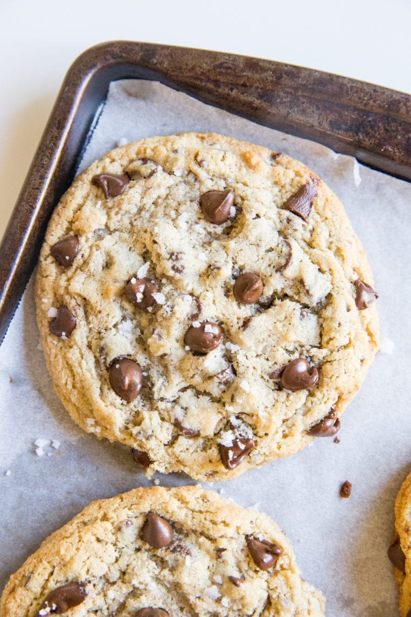 Large baking sheet with giant paleo chocolate chip cookies on top, sprinkled with sea salt.