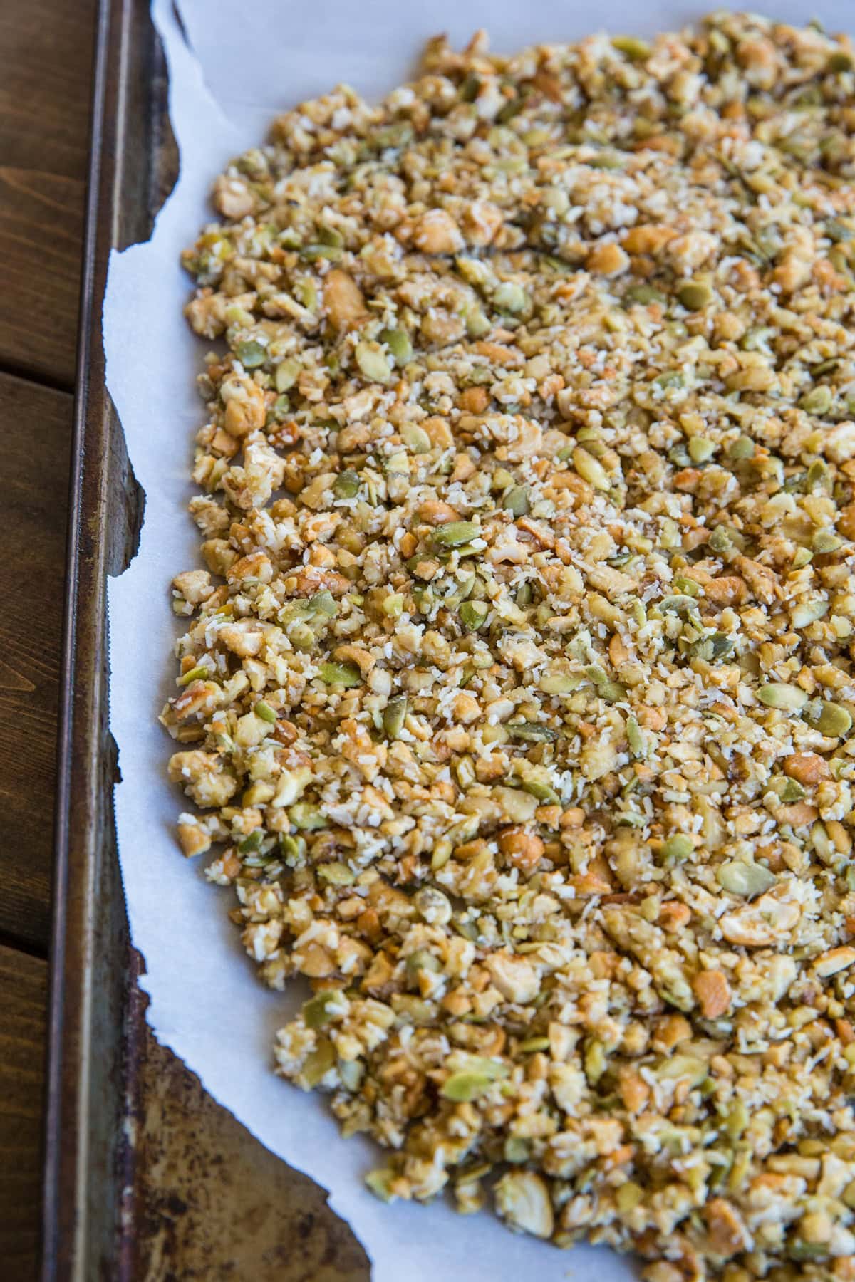Baking sheet with homemade granola on top of a sheet of parchment paper, all stuck together and about to go into the oven.