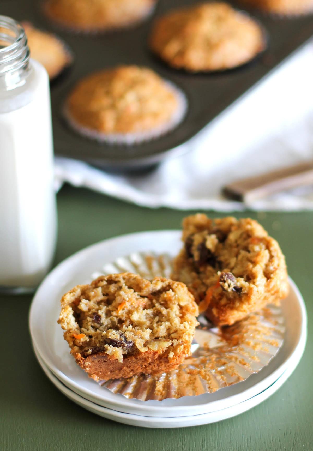 Morning glory muffin sliced in half on a white plate to show the inside and the rest of the muffins in the background.