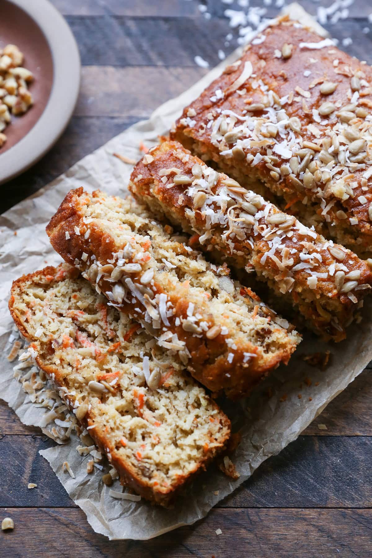 Loaf of morning glory bread cut into thick slices on a sheet of parchment paper on a wooden backdrop.