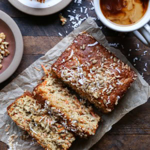 Loaf of morning glory muffin bread on a wooden background, cut into thick slices with a mug of coffee to the side.