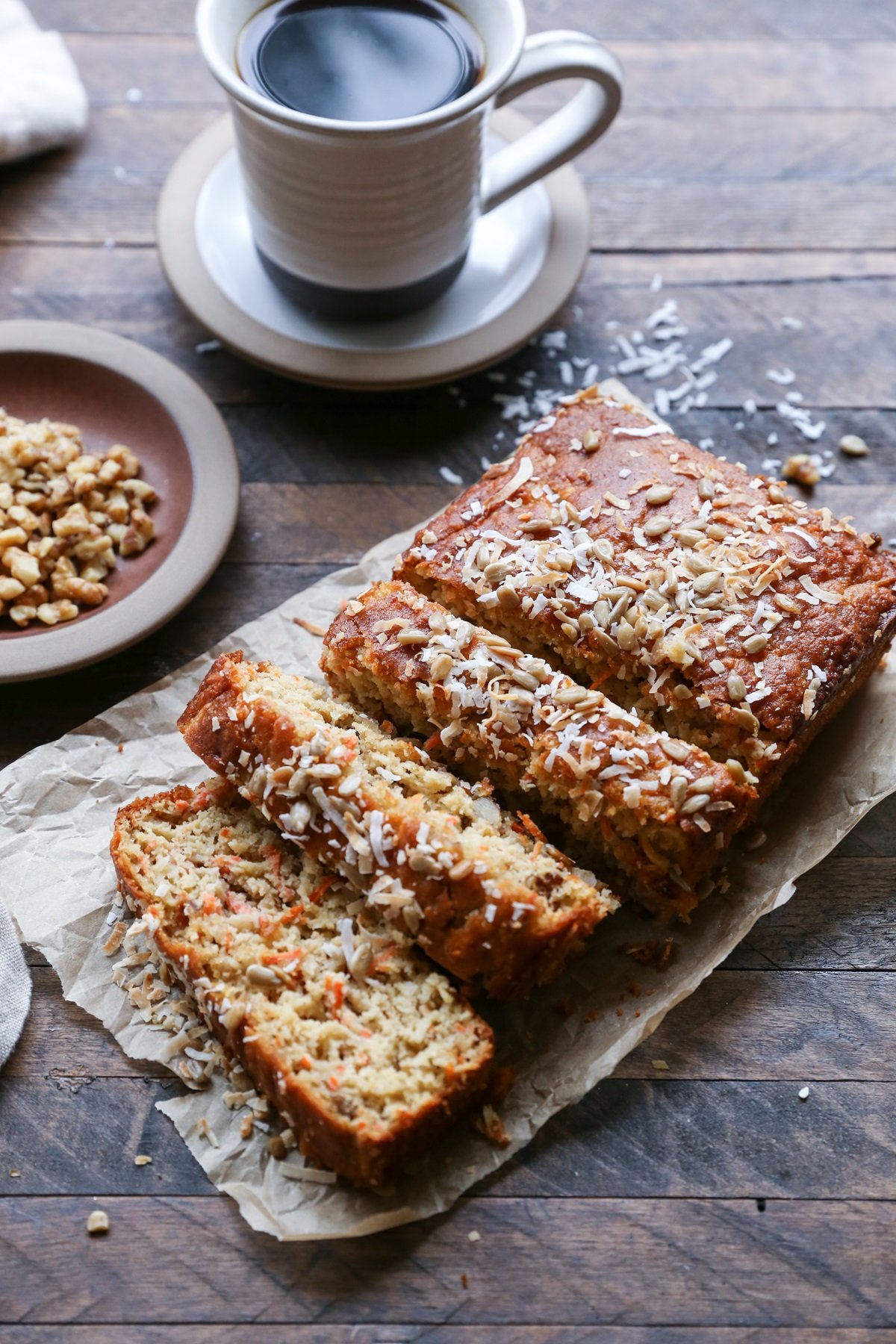 Grain-Free Paleo Morning Glory Quick Bread on a sheet of parchment paper, cut into slices with a mug of coffee in the background.