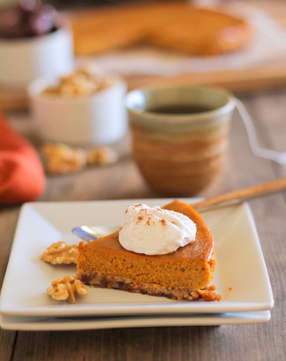 One slice of Paleo Pumpkin Pie on top of two white plates with the rest of the pie in the background.