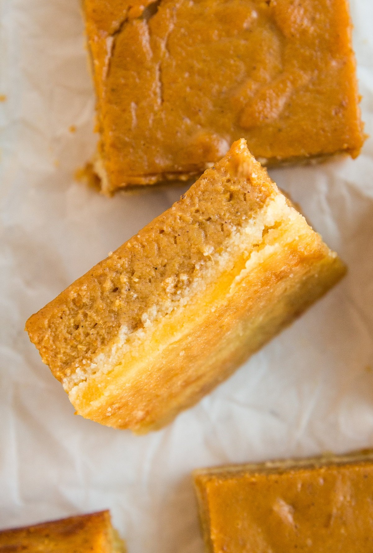 Pumpkin pie bar turned on its side so you can see the layering, with pumpkin pie bars all around.