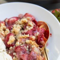 grain-free strawberry crumble in a white bowl with vanilla ice cream and a gold spoon.