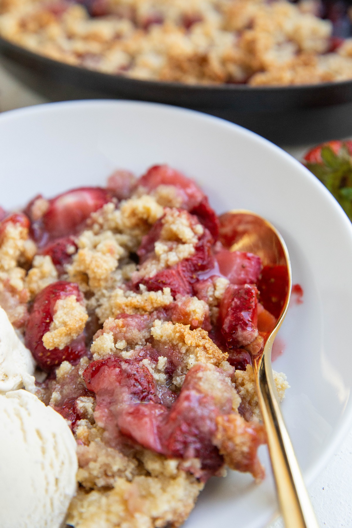 grain-free strawberry crumble in a white bowl with vanilla ice cream and a gold spoon.