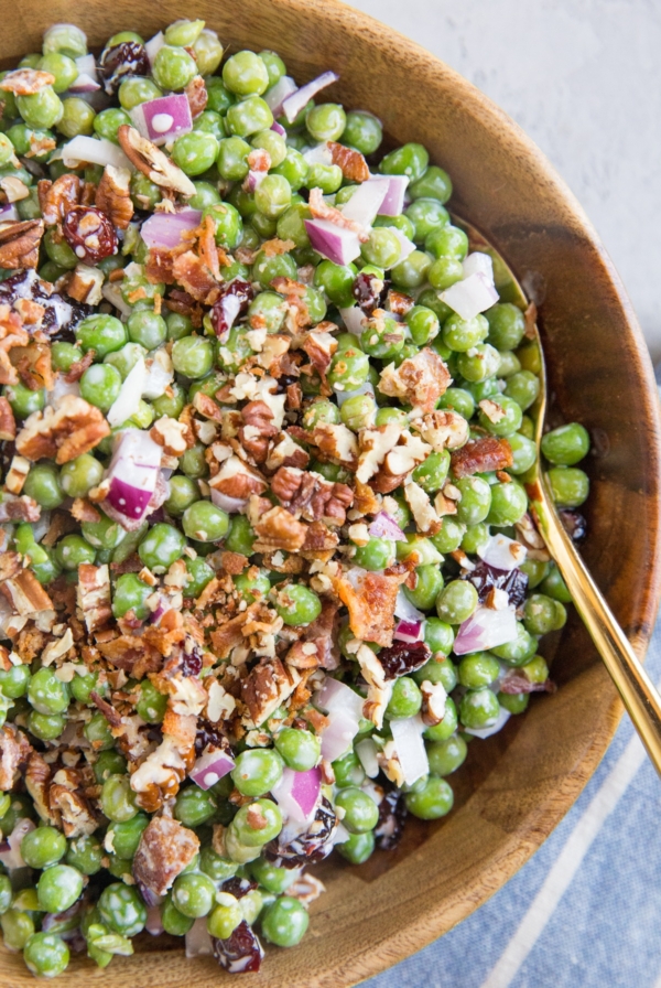 Pea Salad with Bacon, raisins, pecans, and red onion in a large wooden serving bowl with a blue napkin to the side.