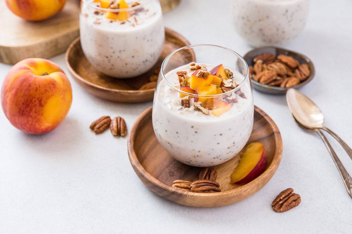 Two glasses full of peach overnight oats with pecans to the side.