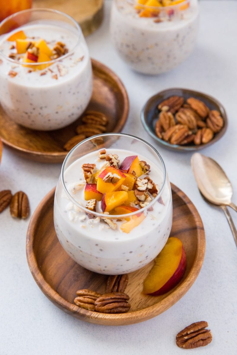 Overnight oats in three glasses with peaches and pecans on top.