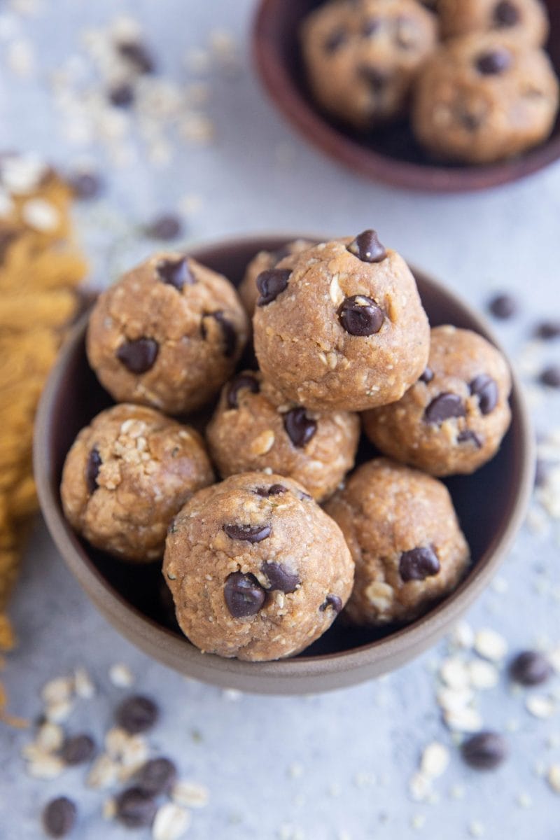 Peanut butter bites in a bowl with chocolate chips and oats sprinkled all around.