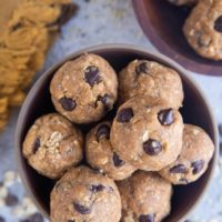 Close up of two bowls with energy balls inside, ready to eat. Chocolate chips and oats sprinkled around the bowls with a golden napkin.