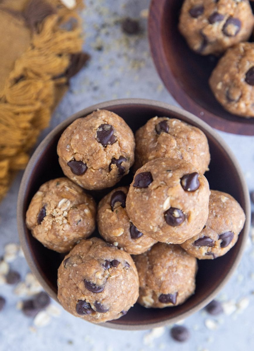 Close up of two bowls with energy balls inside, ready to eat. Chocolate chips and oats sprinkled around the bowls with a golden napkin.