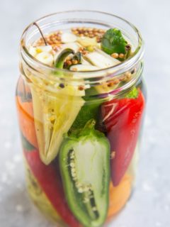 A jar of pickled peppers with jalapeno peppers, habaneros, white peppers, red chiles, etc. Ready to be stored for canning.