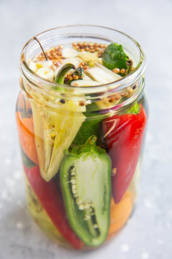 A jar of pickled peppers with jalapeno peppers, habaneros, white peppers, red chiles, etc. Ready to be stored for canning.