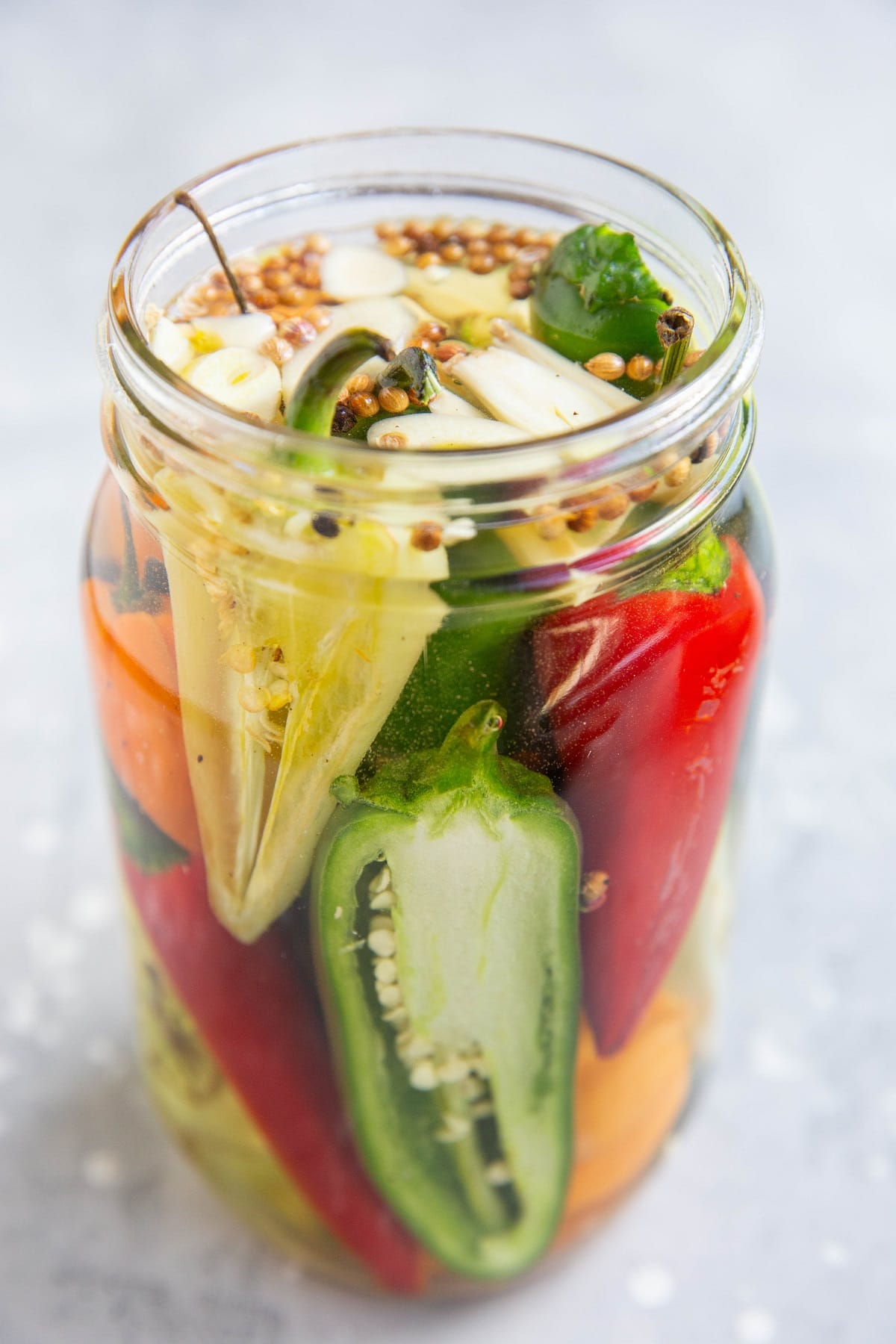 A jar of pickled peppers with jalapeno peppers, habaneros, white peppers, red chiles, etc. Ready to be stored for canning.