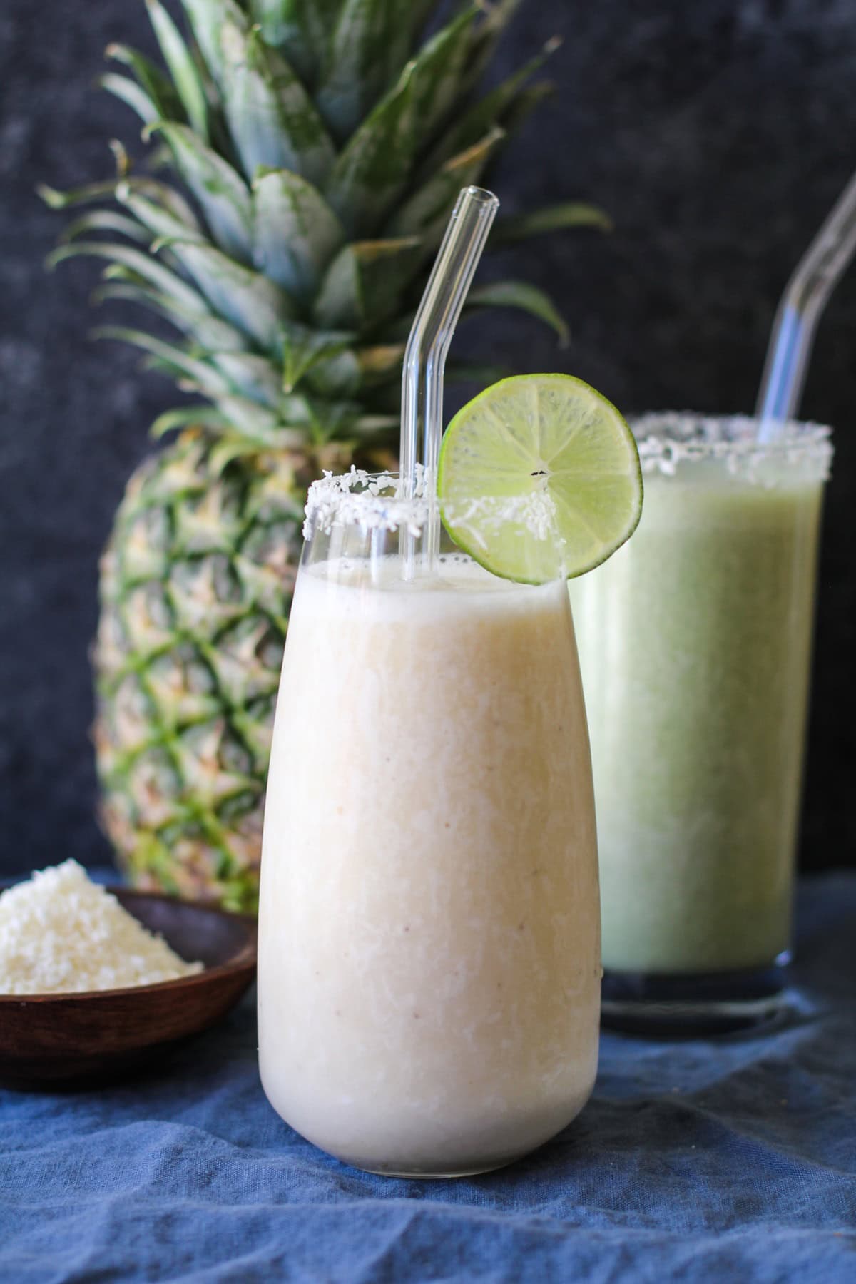 Two glasses of pina colada smoothie rimmed with shredded coconut and slices of lime. Ready to drink.