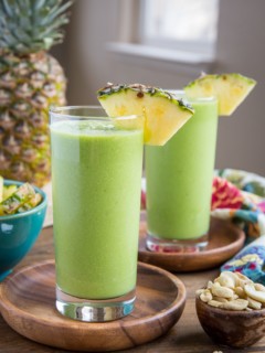 Two glasses of protein smoothies on a wooden background with a small bowl of cashews to the side, ready to sip on.