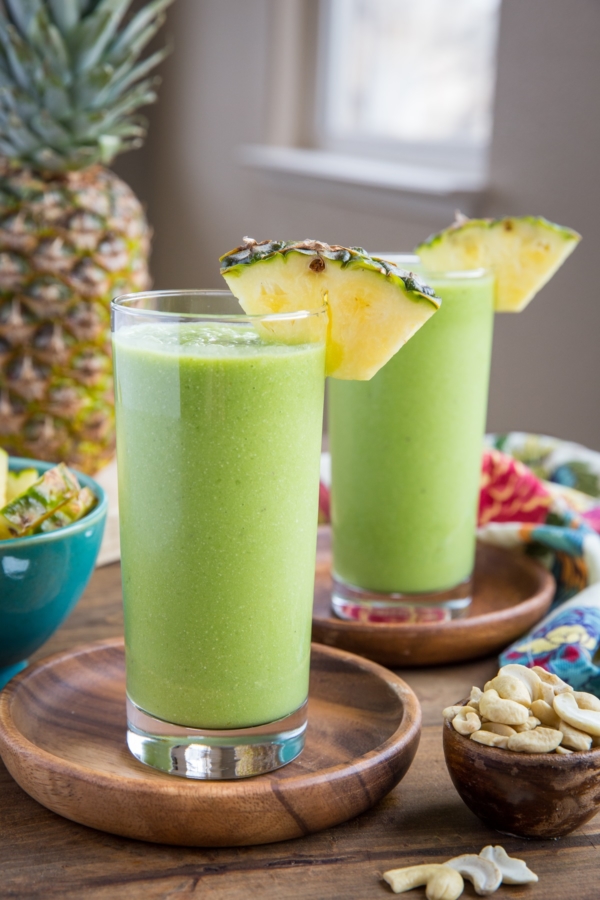 Two glasses of protein smoothies on a wooden background with a small bowl of cashews to the side, ready to sip on.