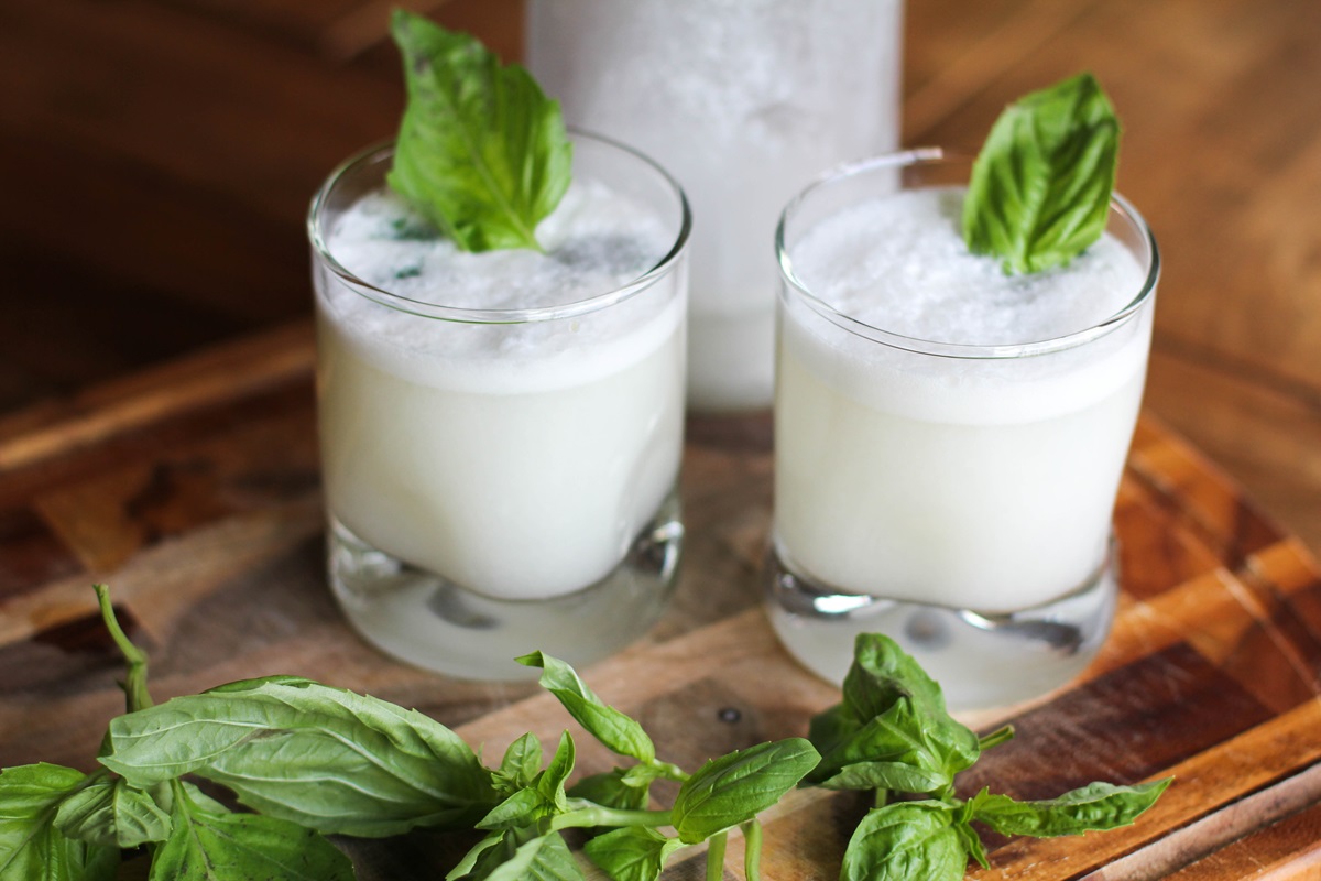 closeup glass of coconut basil ginger beer with a glass and bottle in the background