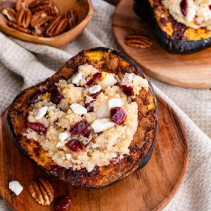 Acorn Squash stuffed with quinoa, pecans, goat cheese, dried cranberries sitting on a wooden plate.