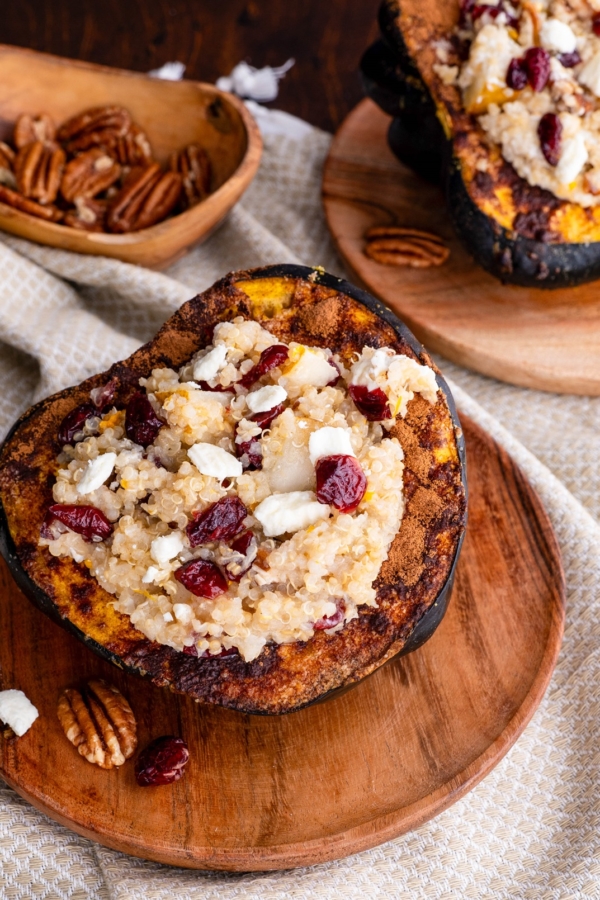 Acorn Squash stuffed with quinoa, pecans, goat cheese, dried cranberries sitting on a wooden plate.