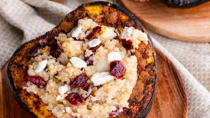 Acorn Squash stuffed with quinoa, pecans, goat cheese, dried cranberries sitting on a wooden plate.