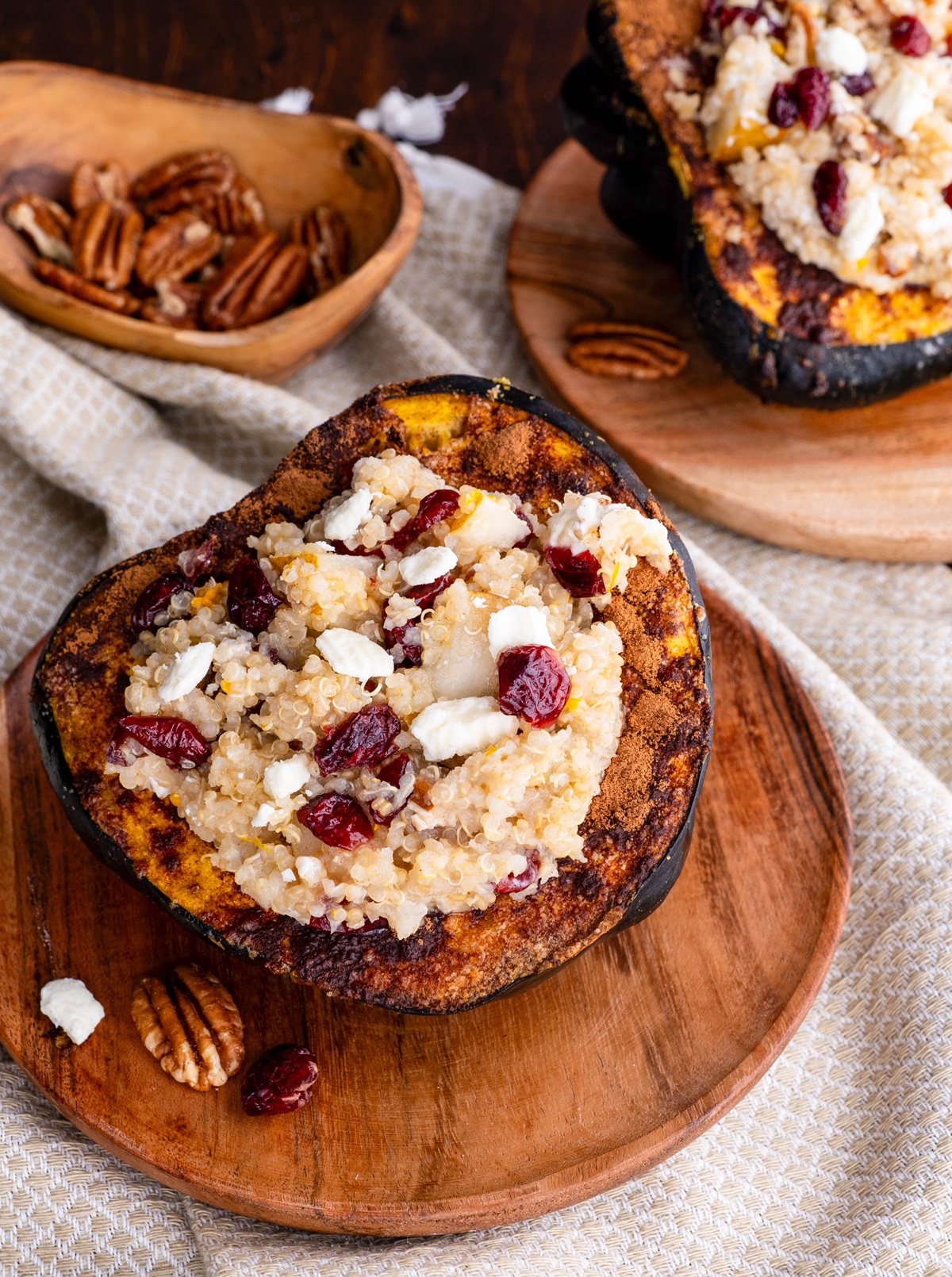 Acorn Squash stuffed with quinoa, pecans, goat cheese, dried cranberries sitting on a wooden plate.