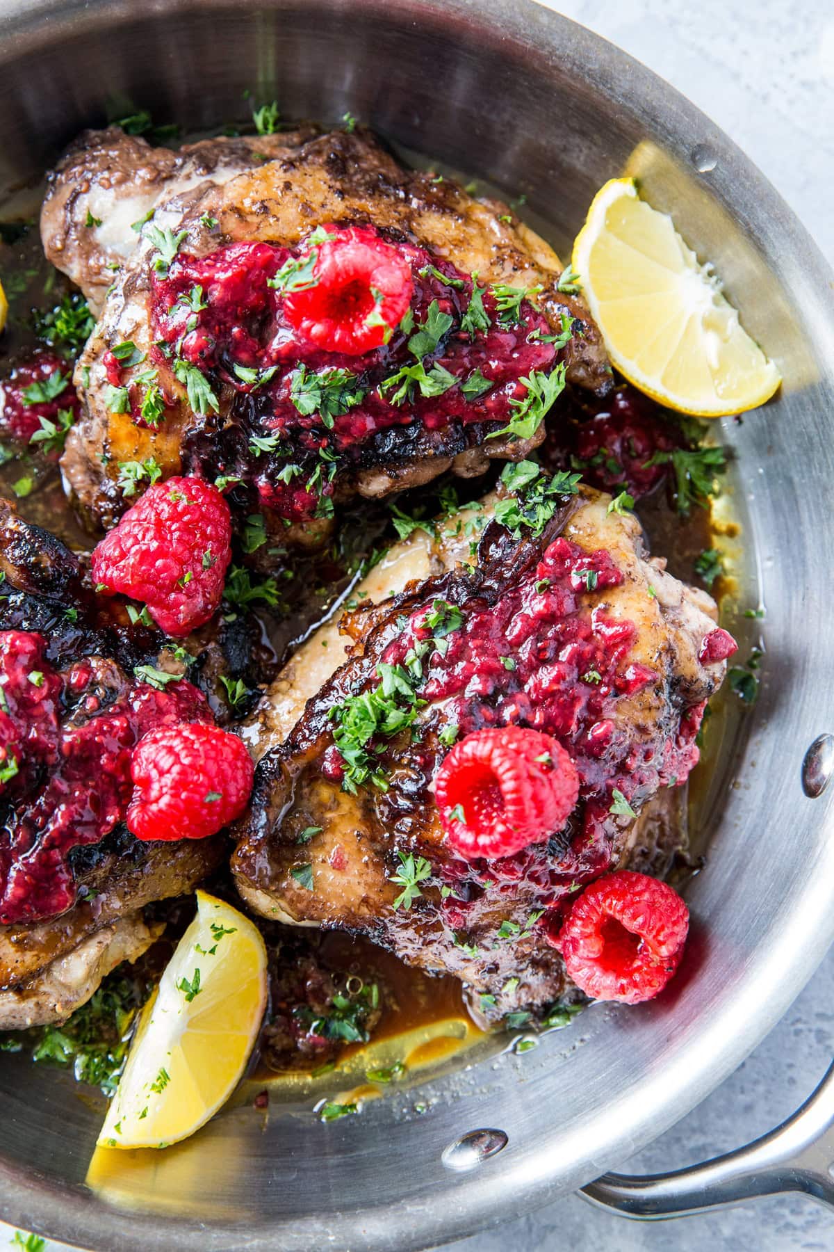 Raspberry Balsamic Chicken in a stainless steel skillet - golden brown crust with raspberry preserves on top and limes to the side.